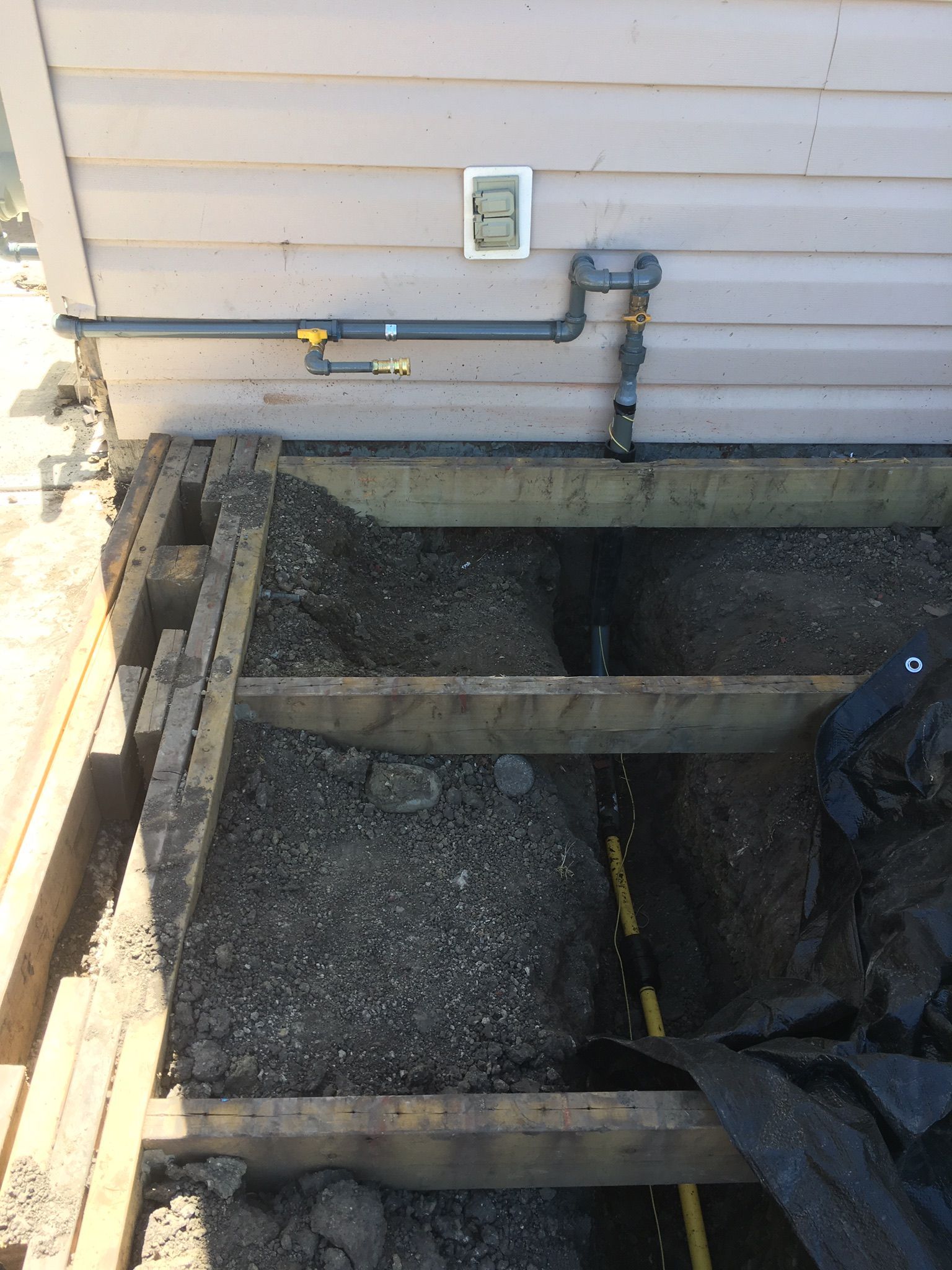 A hole in the ground next to a house with pipes coming out of it.