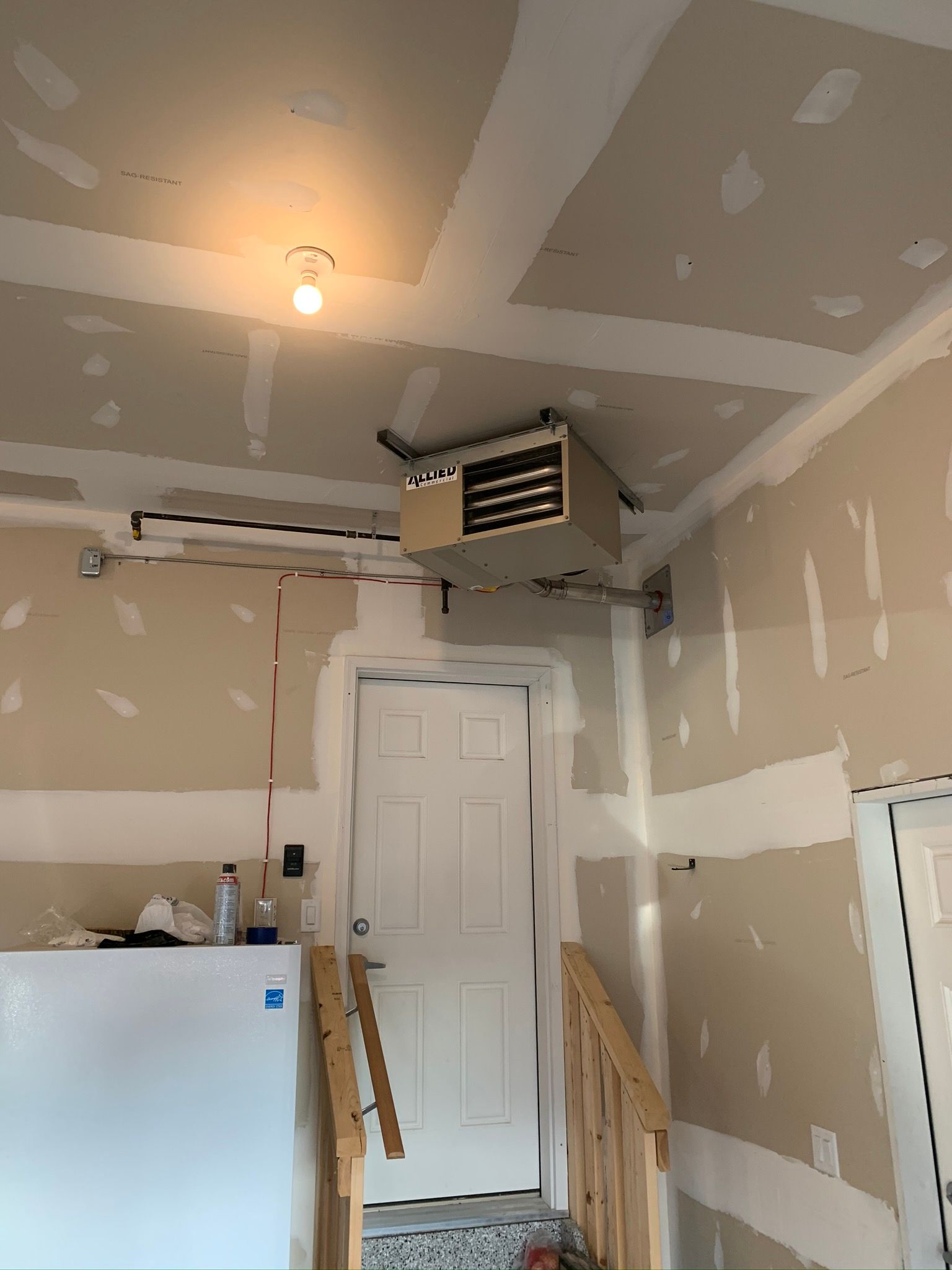 A room with a heater hanging from the ceiling and a door.