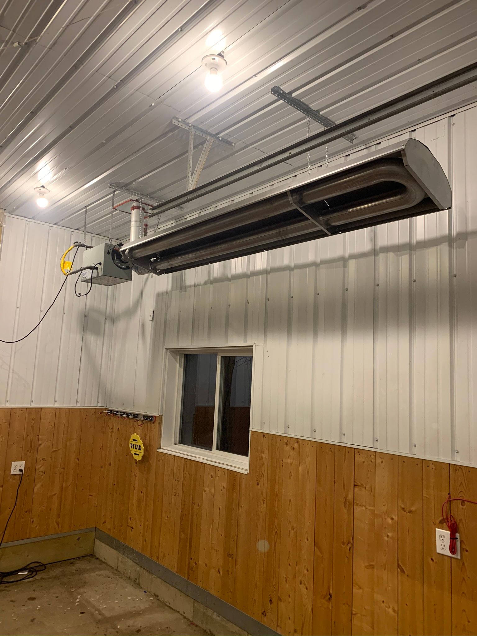 A large heater is hanging from the ceiling of a building next to a window.