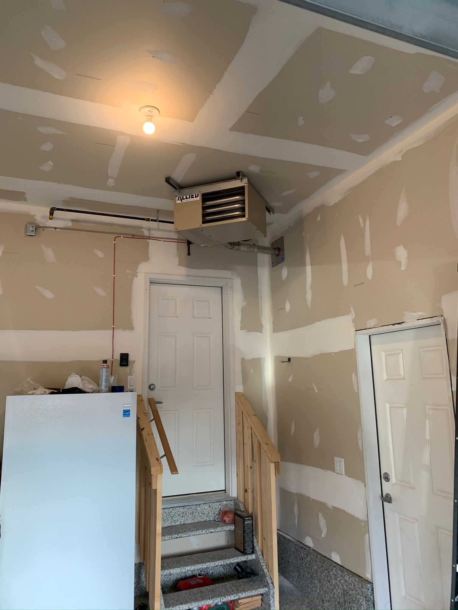A garage with stairs leading up to a door and a refrigerator.