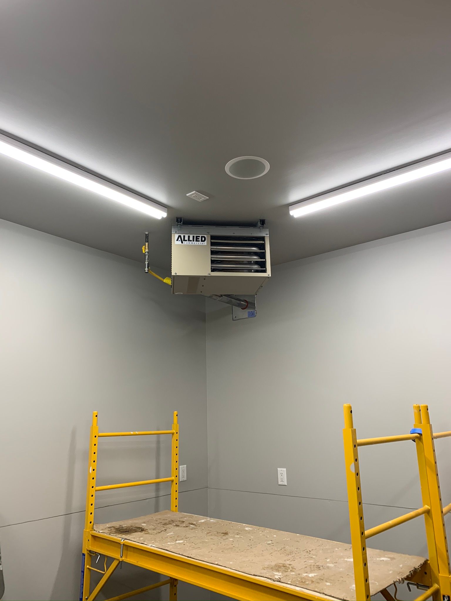 A room with a scaffolding and a heater hanging from the ceiling.