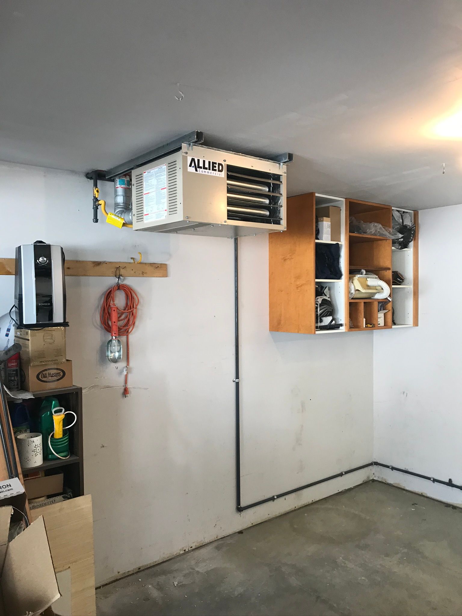 A garage with a heater hanging from the ceiling and shelves.