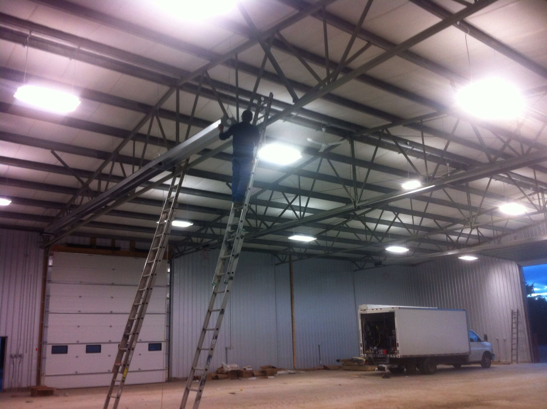 A man on a ladder in a warehouse with a truck in the background