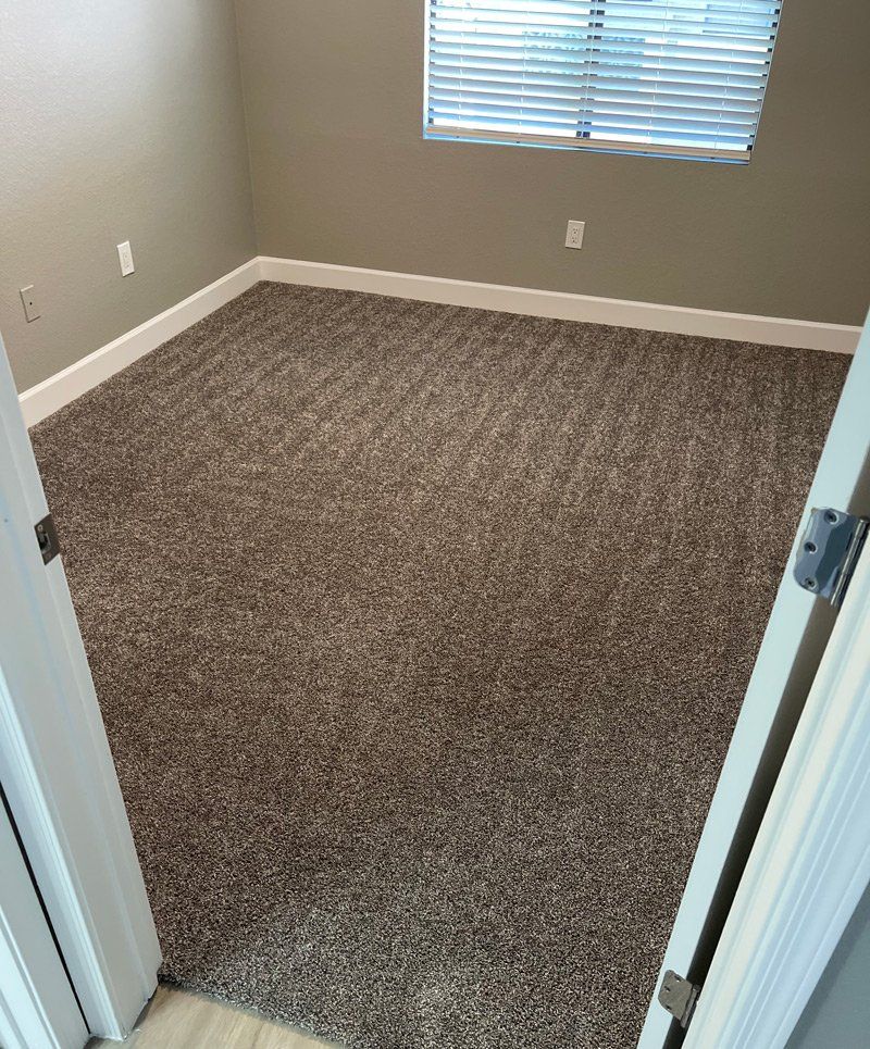 Empty bedroom with neutral-toned carpet, white trim, and a window with blinds.
