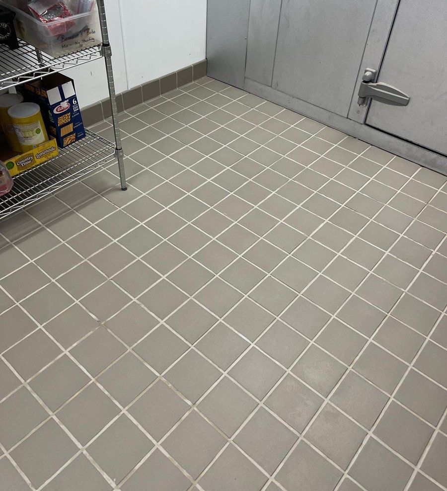 Gray tiled floor in a room with a metal shelf of food items and a cold storage door.