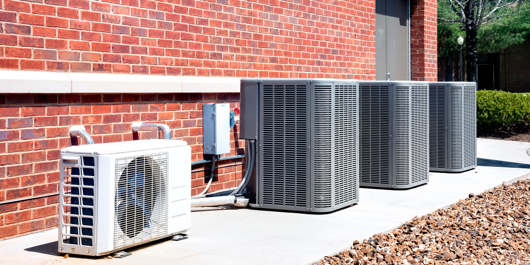 Several outdoor air conditioning units beside a brick building in sunlight.