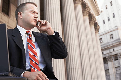 A man in a suit and tie is talking on a cell phone in front of a building.