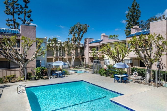 A large swimming pool surrounded by tables and chairs in front of a building.