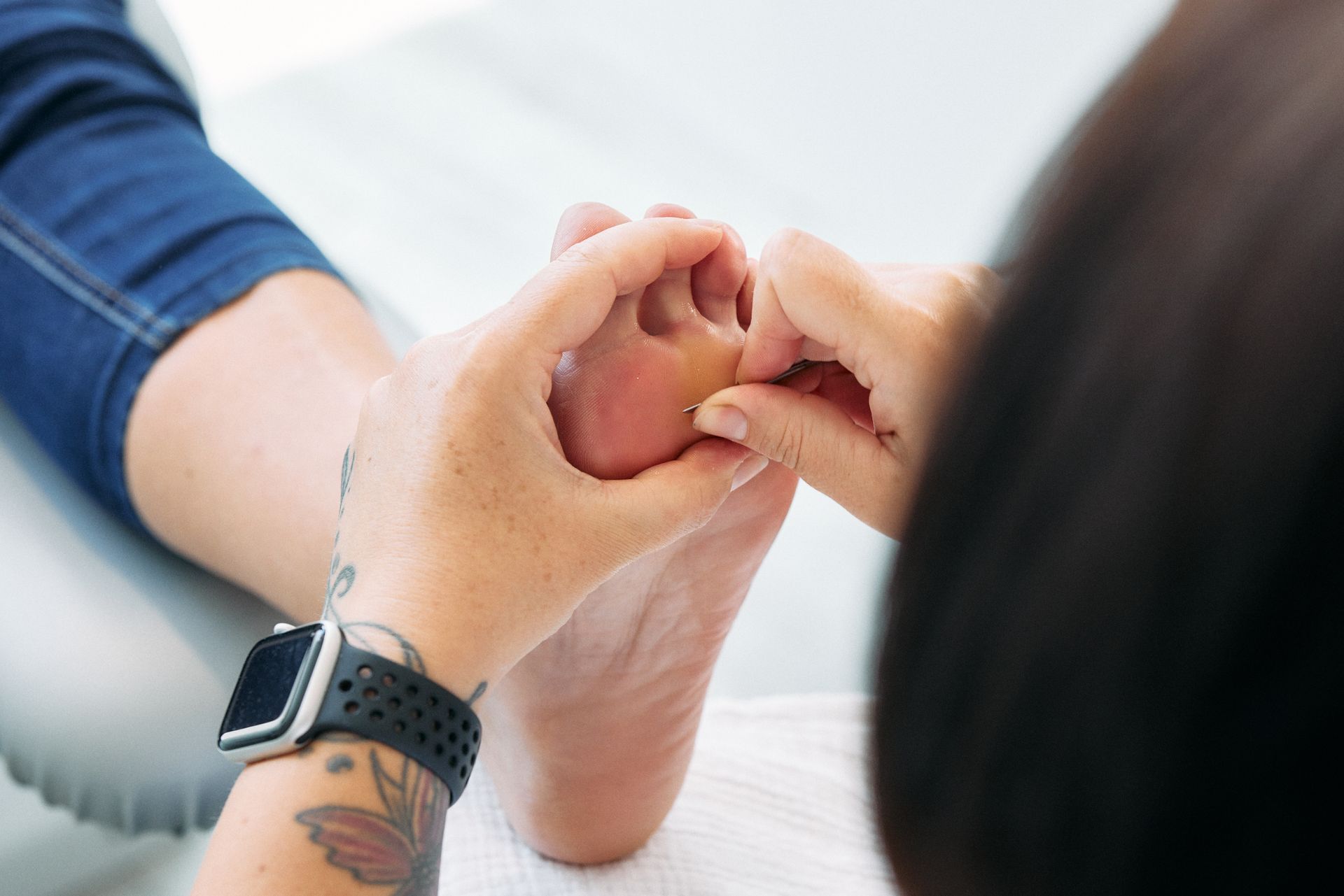 Eine Frau , die eine Uhr am Handgelenk trägt , massiert den Fuß einer Person .