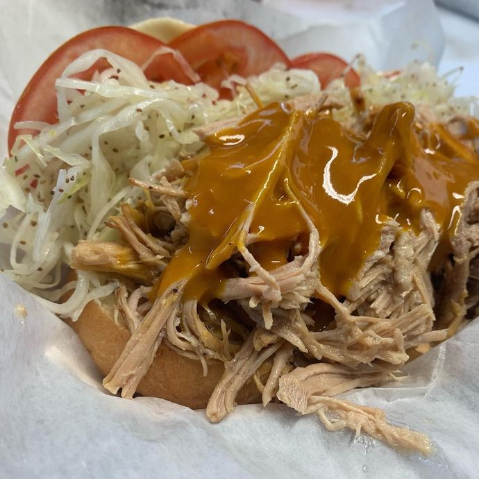 A pulled pork sandwich with tomatoes and cabbage on a bun