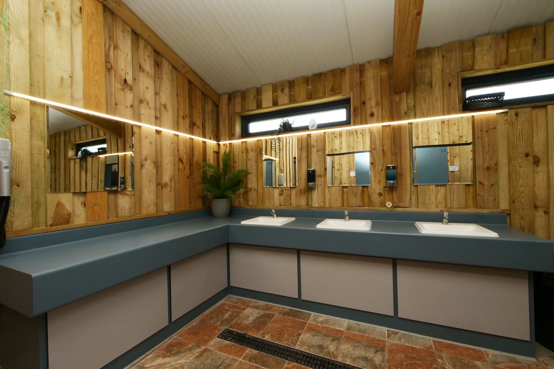 Modern wash room with double sinks, large mirrors, wood-paneled walls, and blue countertops