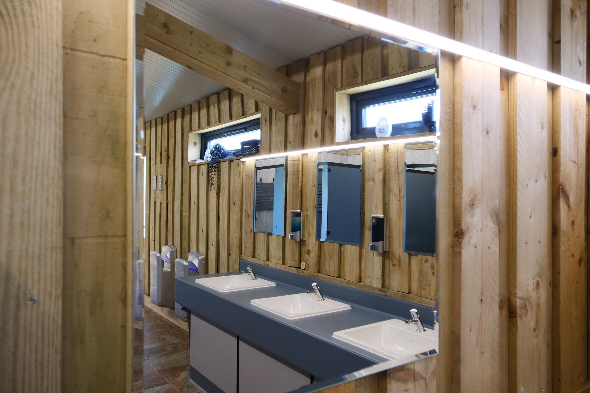 Wood-paneled restroom with double sinks, mirrors, and a long countertop under skylights.