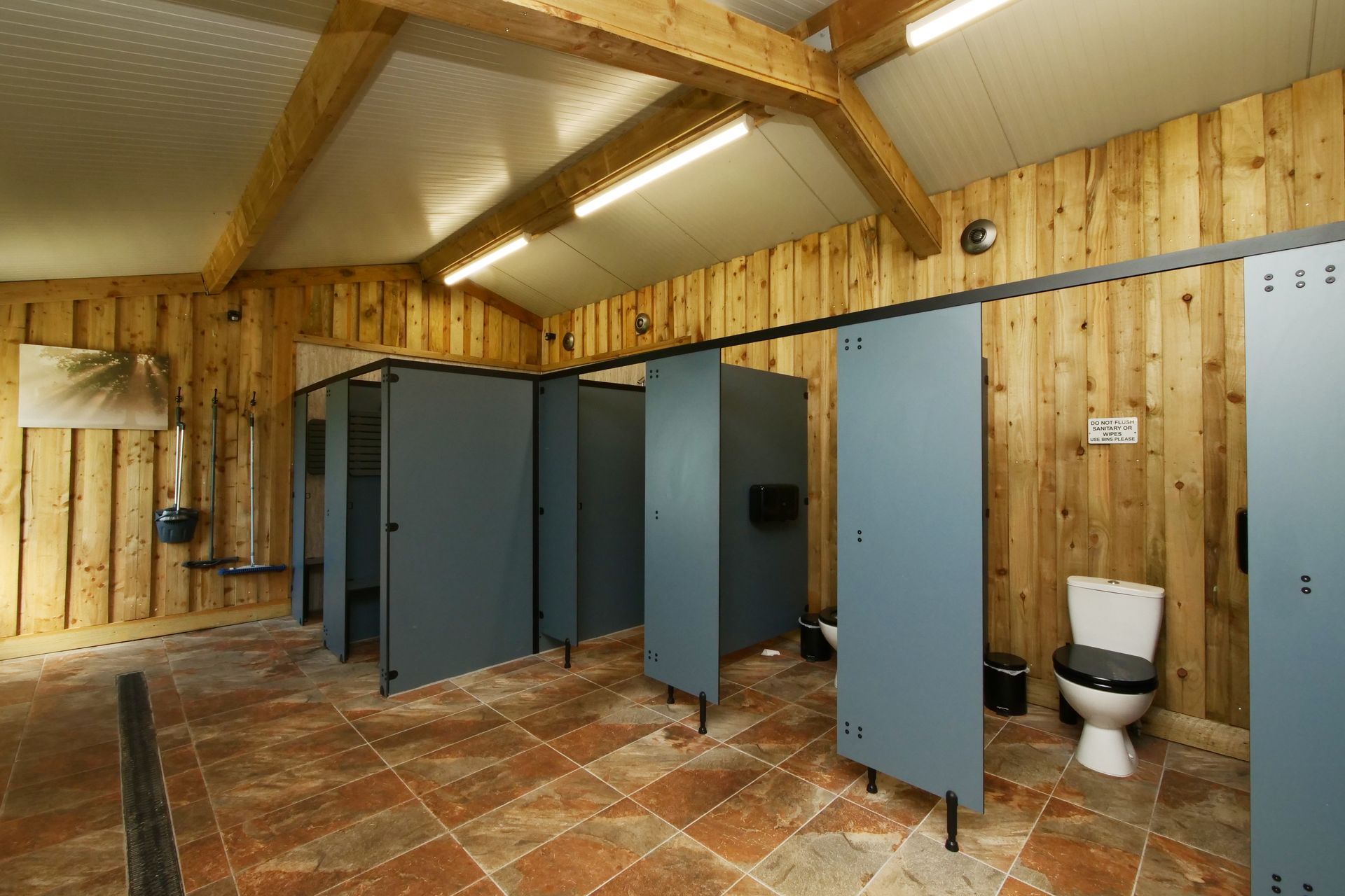 Rustic shower block with blue stall doors and a toilet in a wooden building with tiled floor.