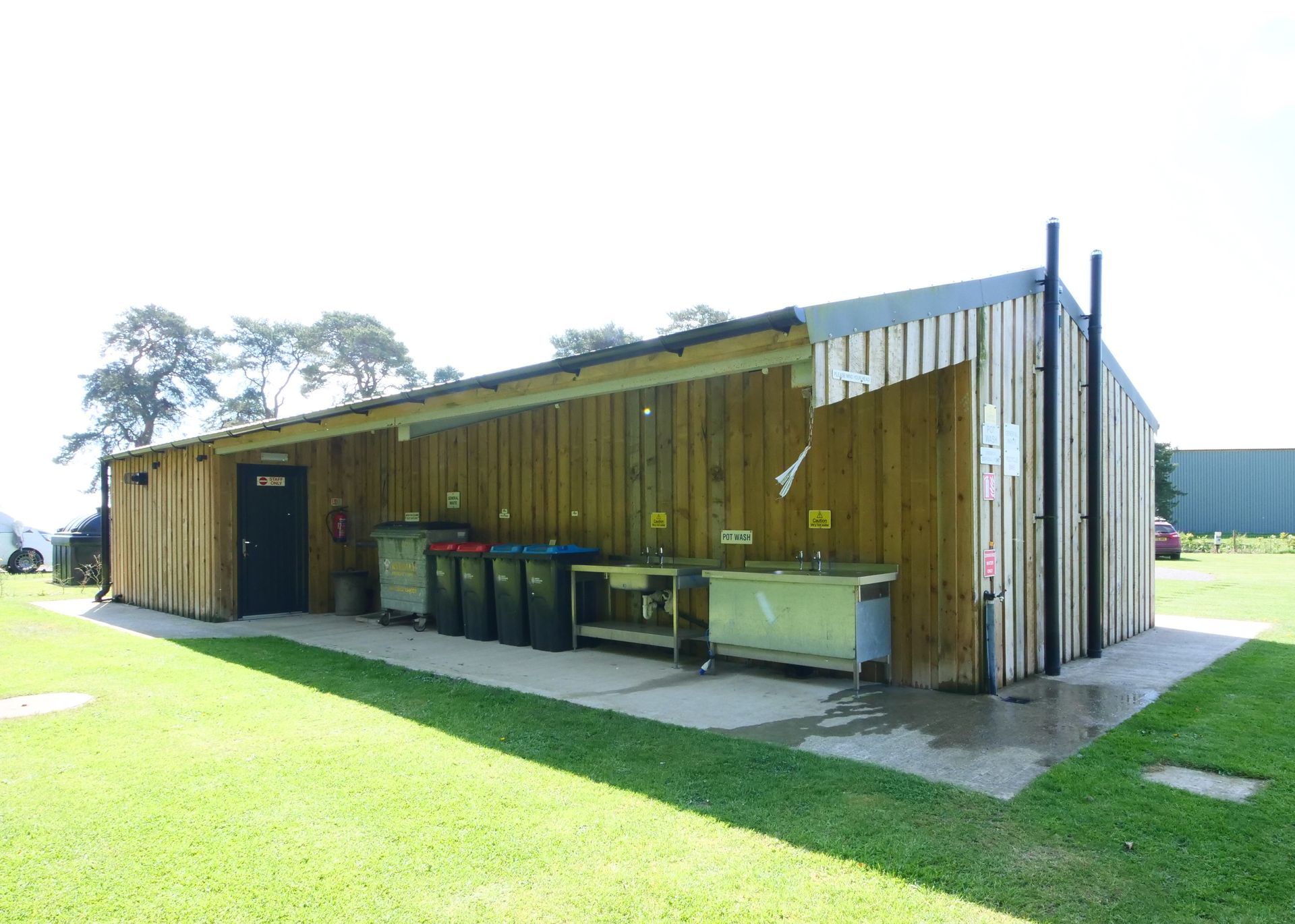 Long wooden shower block building with outdoor bins and picnic tables beside a grassy lawn