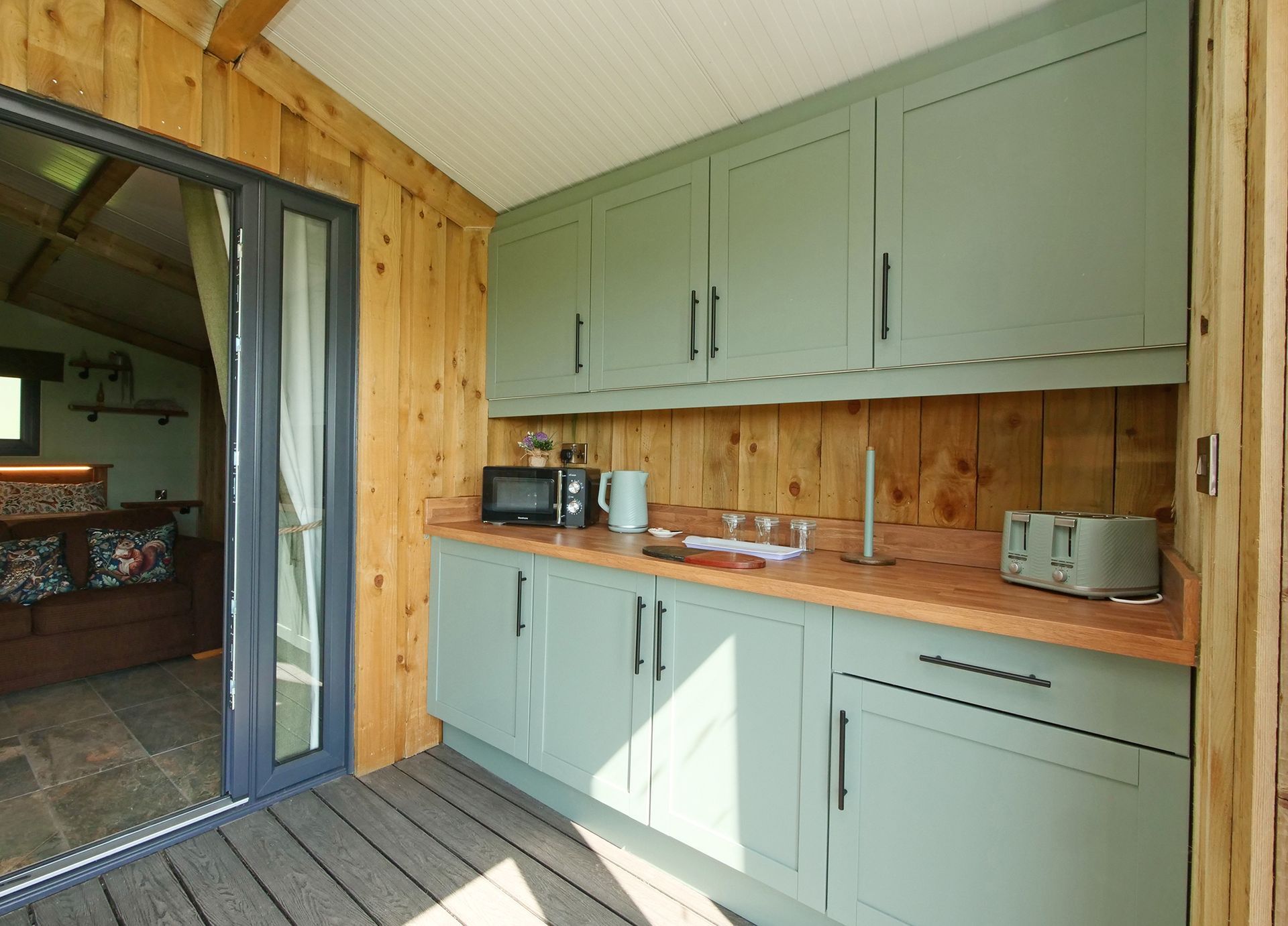 Pod kitchenette with sage green cabinets, wood paneling, countertop appliances, and a sliding glass door