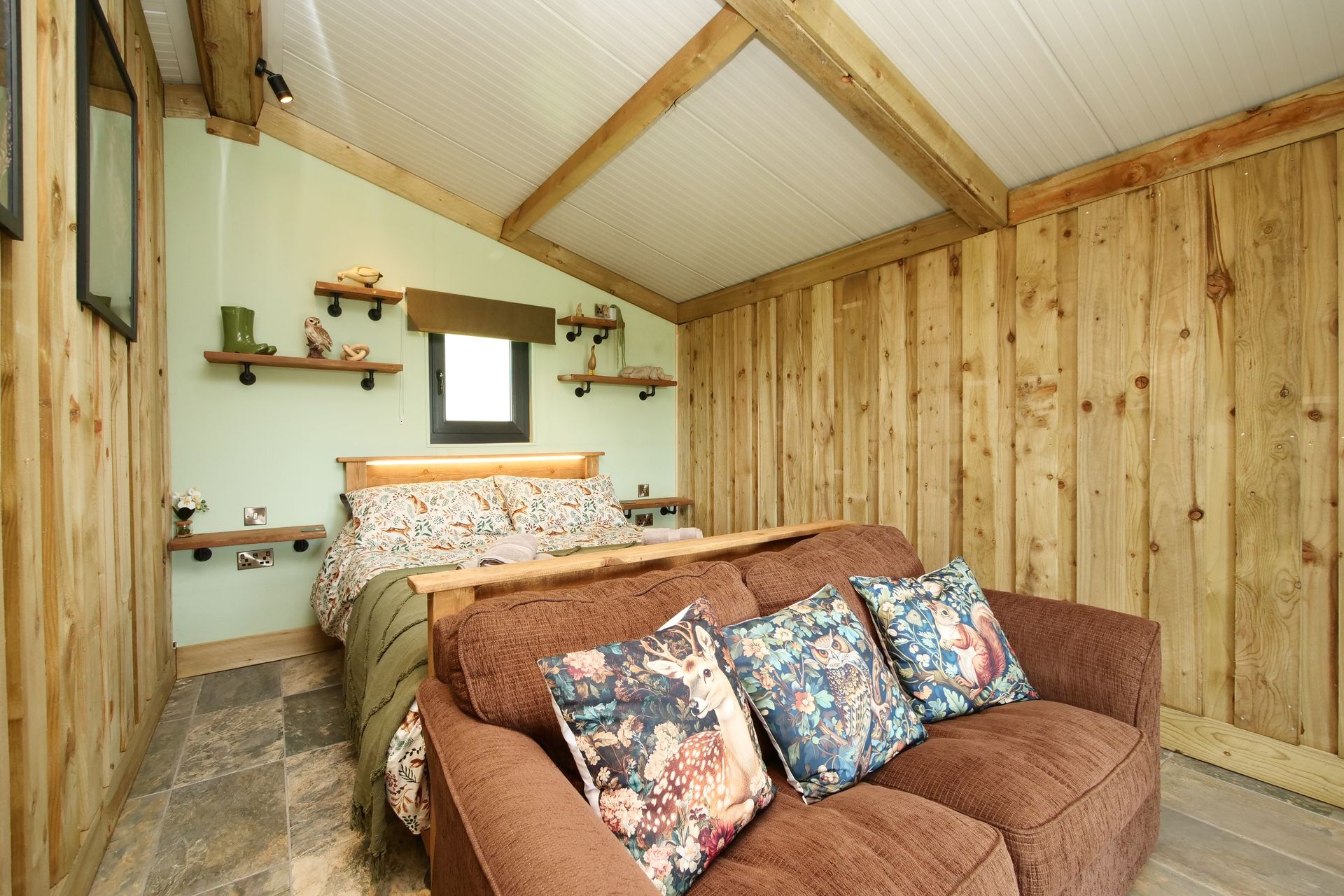 Cozy loft bedroom with wood-paneled walls, a bed, and a brown couch with floral pillows.
