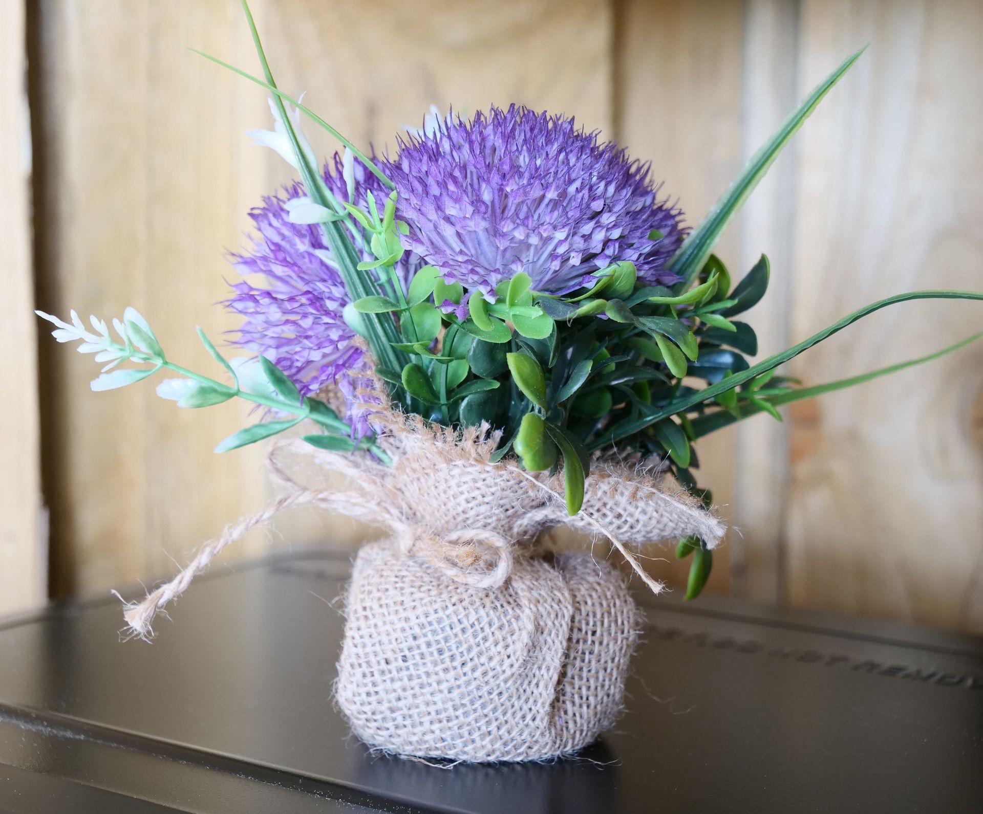 Purple flower arrangement in a burlap-wrapped pot on a dark table