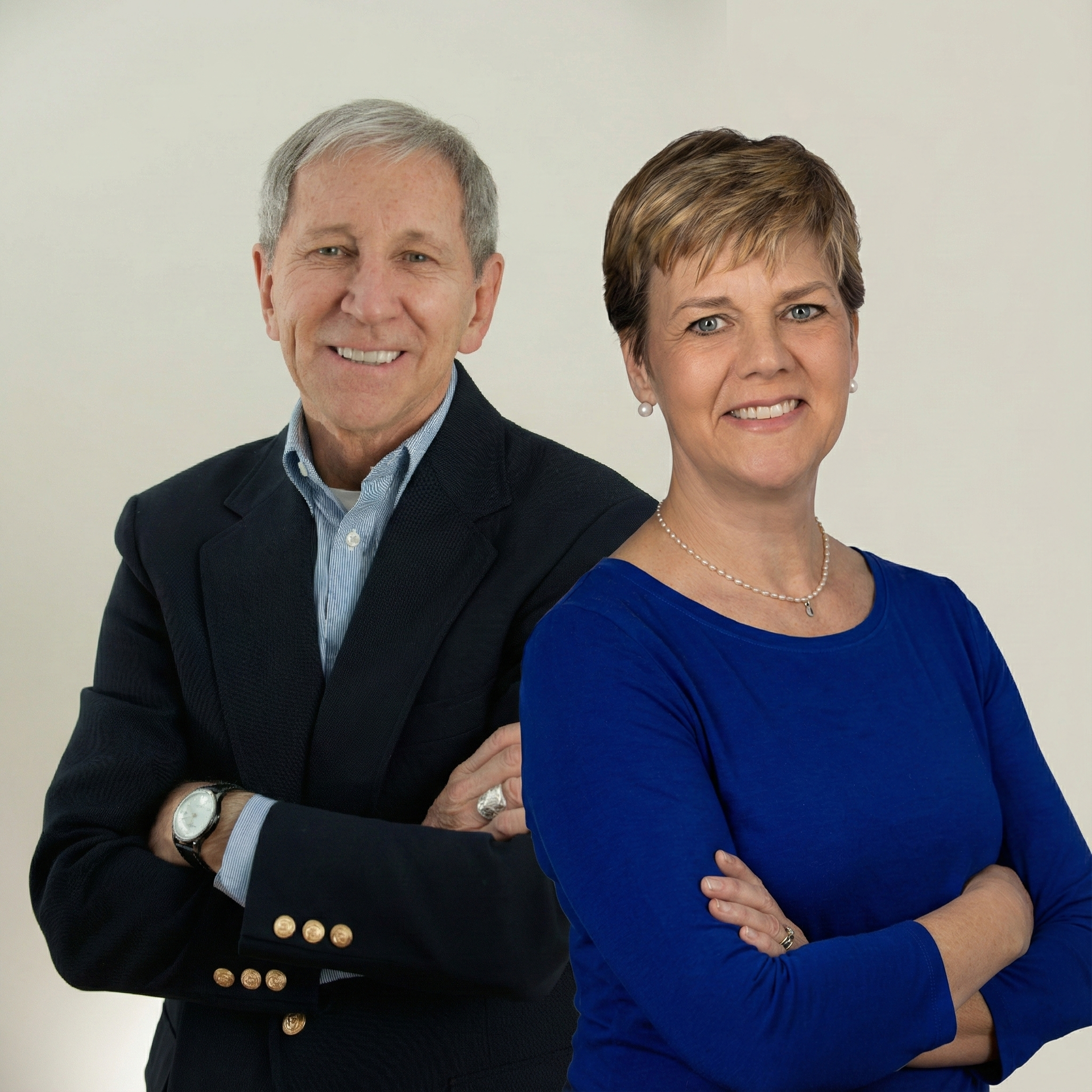 Smiling man and woman pose, arms crossed. Man in blazer and blue shirt. Woman in blue shirt.