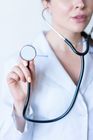 Doctor in white coat holding a stethoscope, cropped close-up against a light background