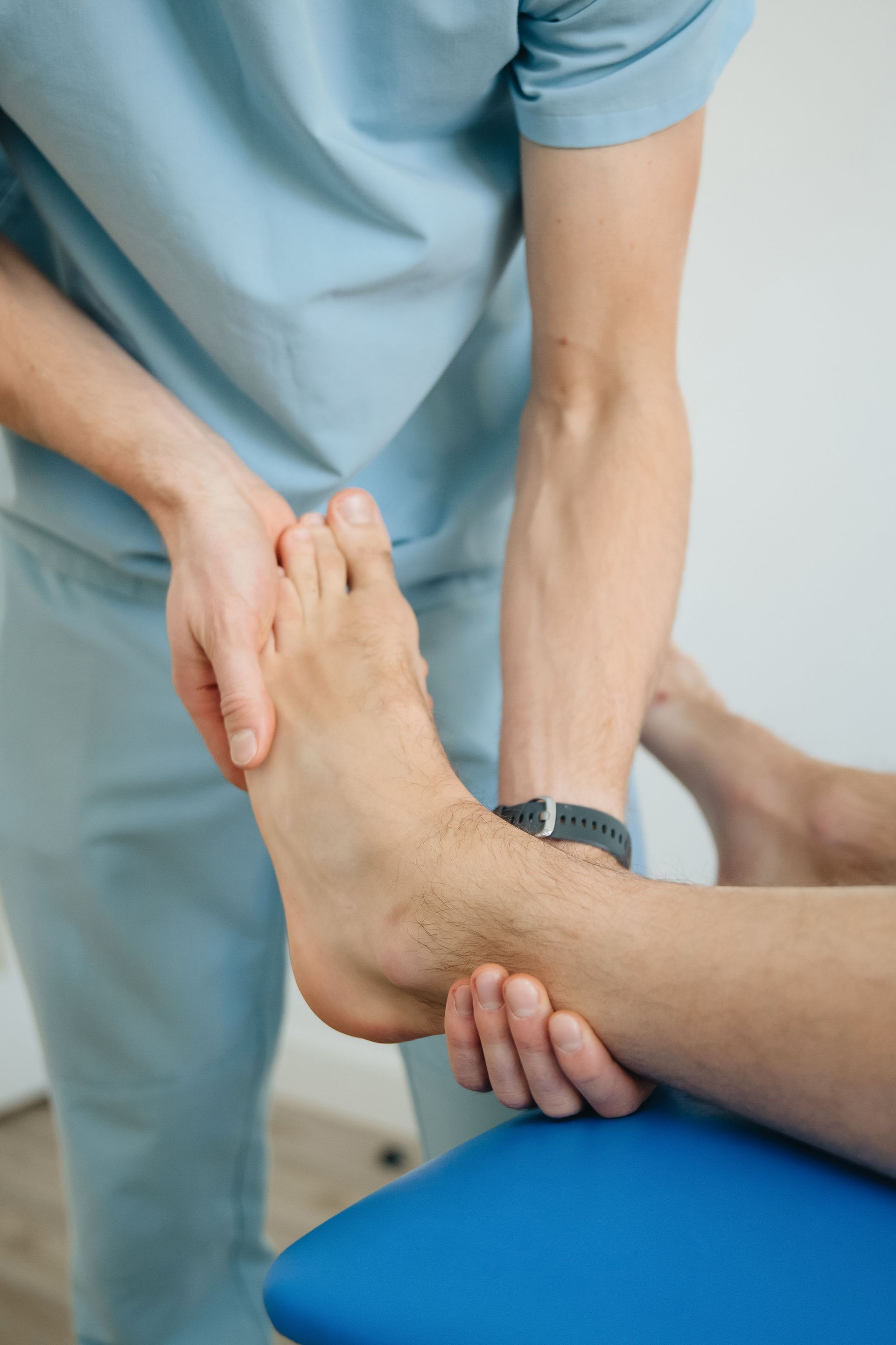 Physical therapist stretching a patient’s foot in a clinic, with a blue treatment table.