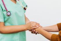Nurse in green scrubs holding a patient's hand in a comforting gesture