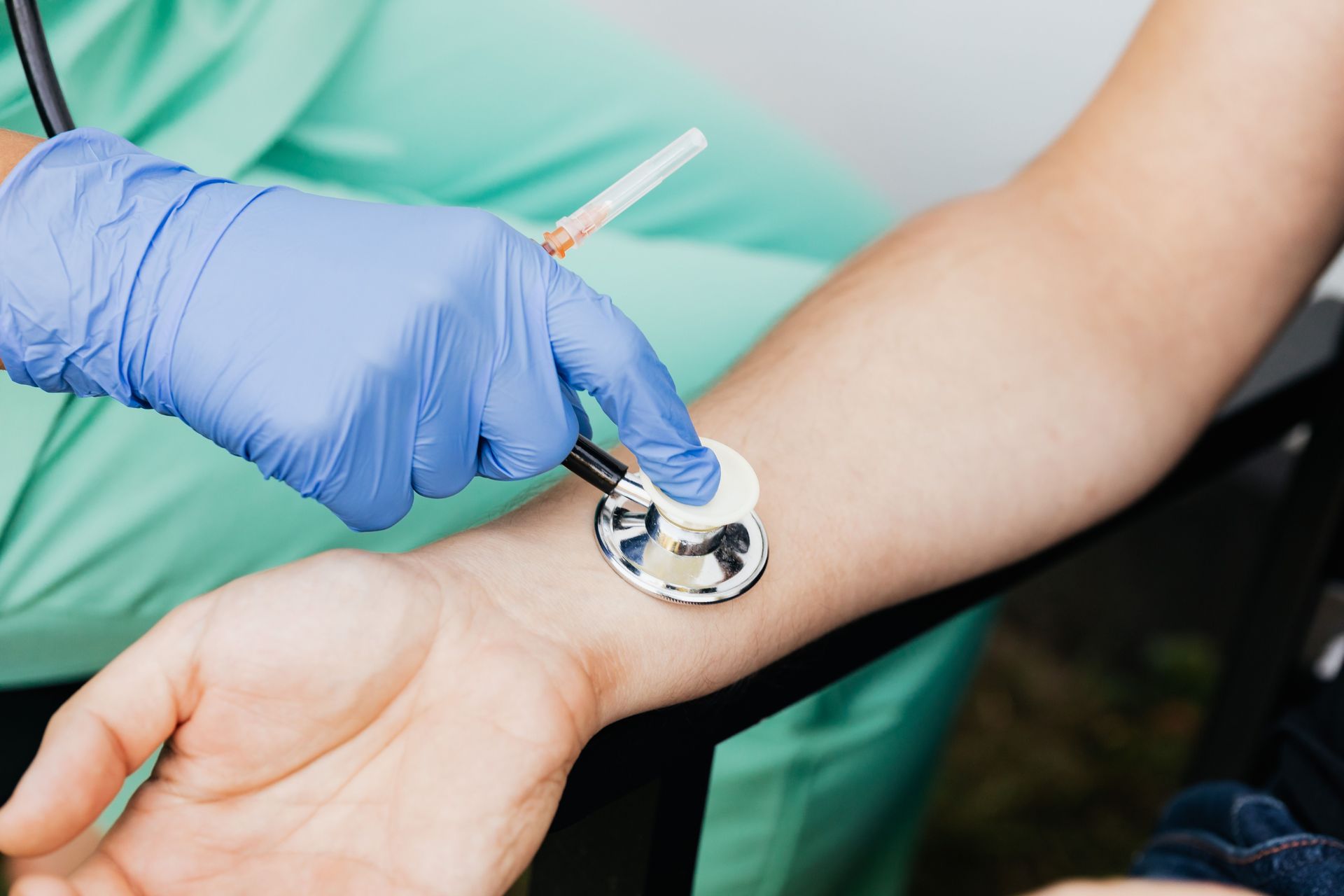 Gloved clinician taking a pulse at a patient’s wrist with a stethoscope