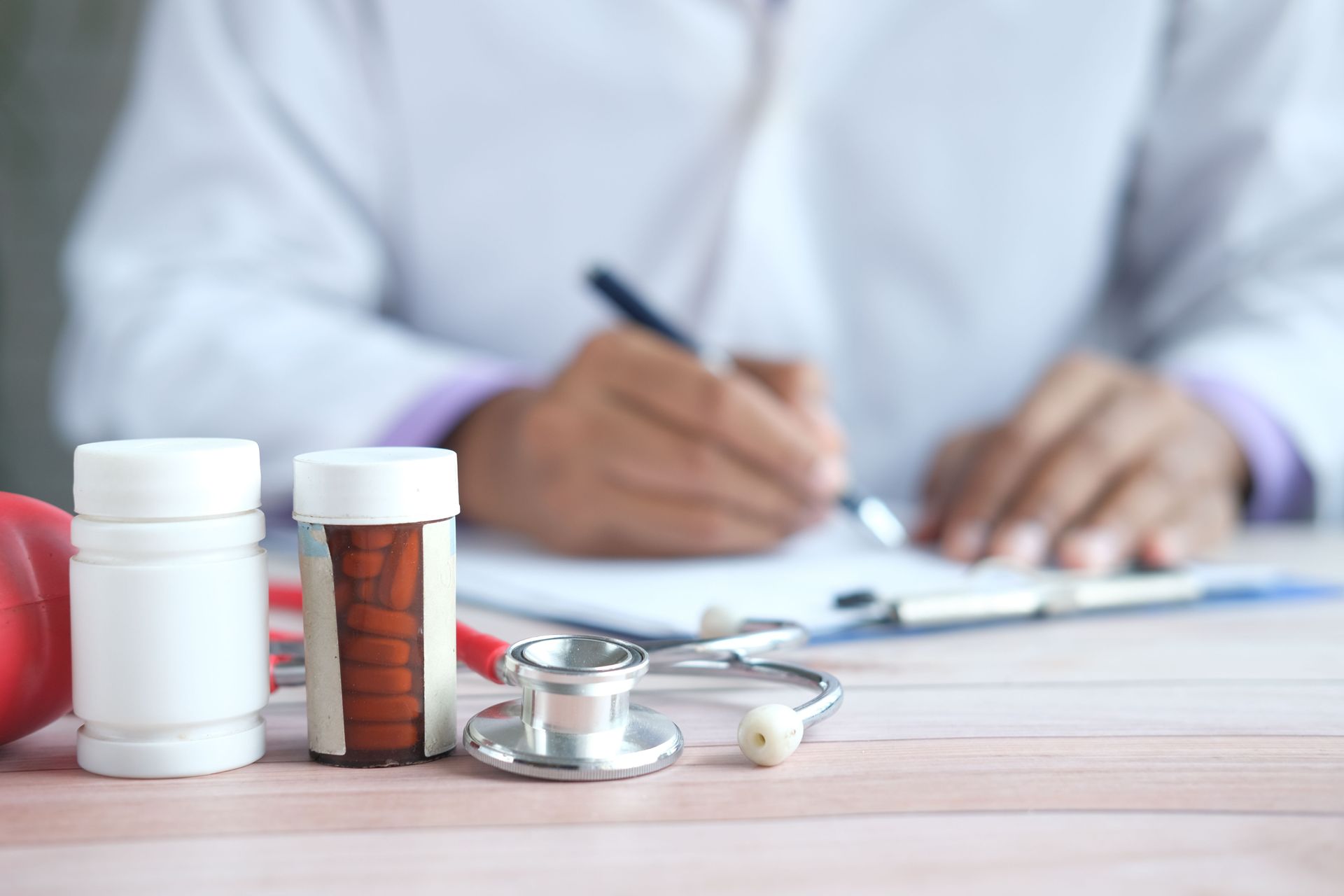 Doctor writing with prescription bottles and stethoscope on desk