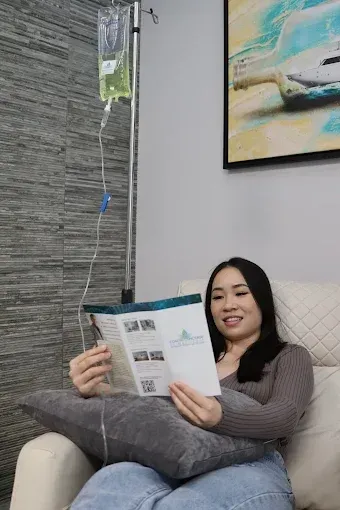 Woman relaxing on a beige sofa, reading a magazine beside a hanging IV drip.