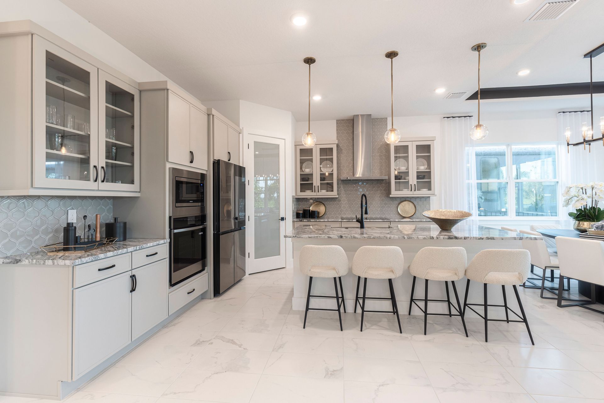 Modern kitchen with gray cabinets, island with stools, stainless steel appliances, and large windows.