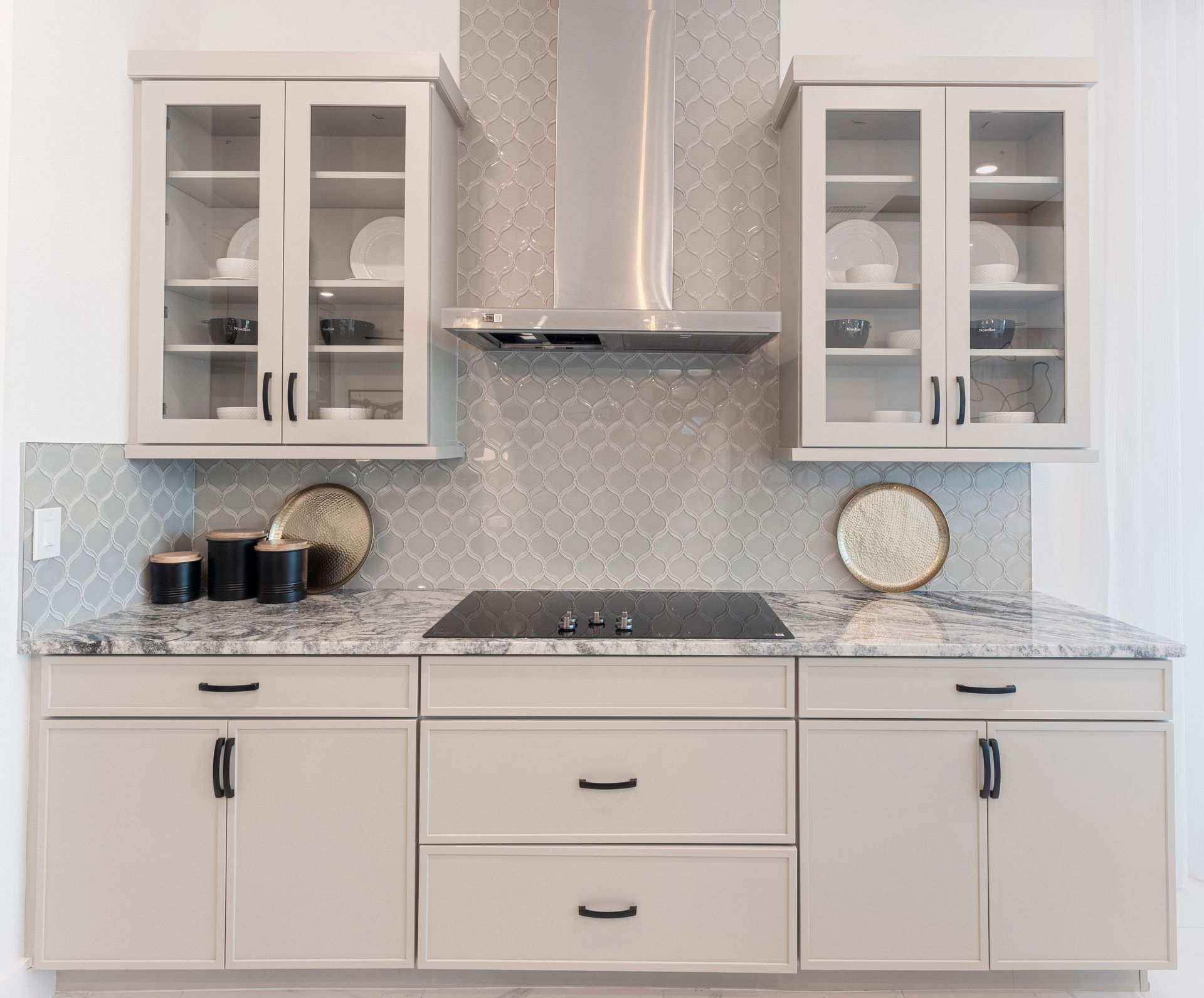 Kitchen with gray cabinets, a stainless steel range hood, and light-colored backsplash.