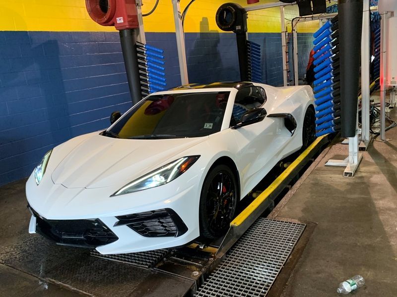 A white corvette is being washed in a car wash.