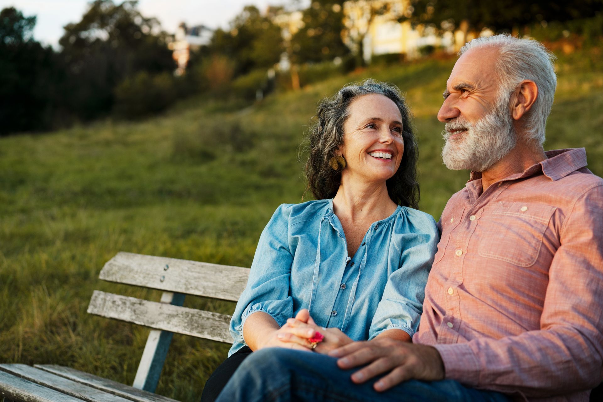 A man and a woman are sitting on a park bench holding hands.