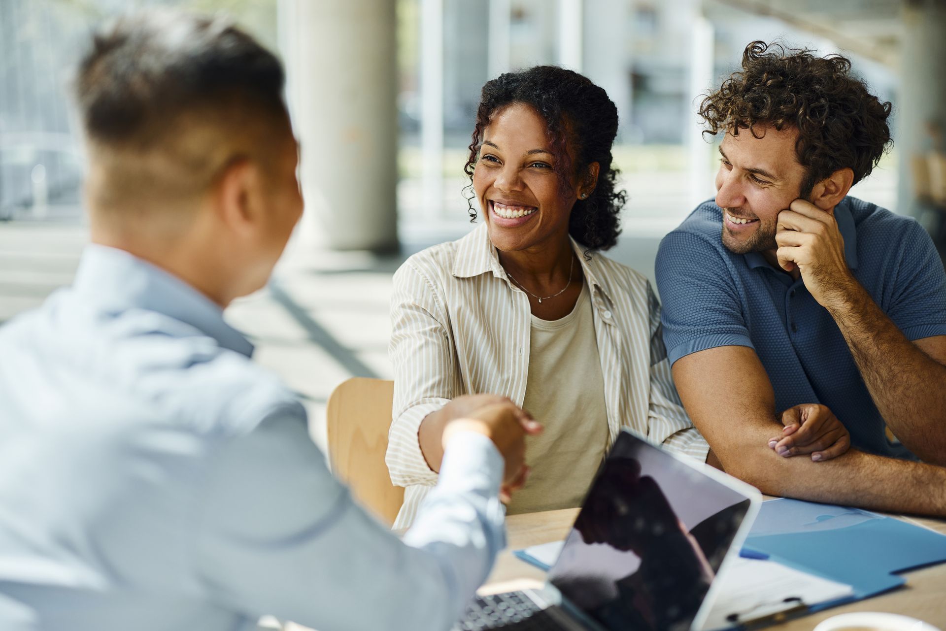 A man is shaking hands with a woman while sitting at a table with a laptop.