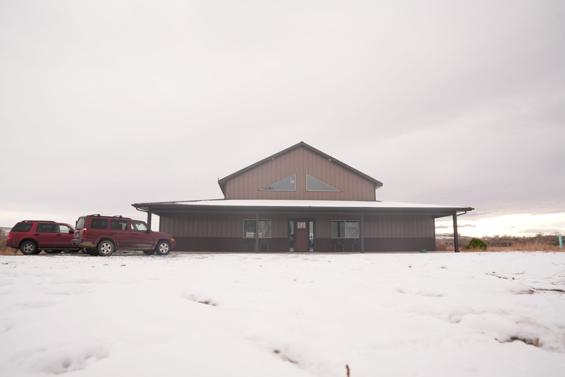 Two cars are parked in front of a building in the snow.