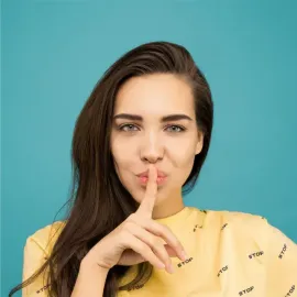 A woman in a yellow shirt is holding her finger to her lips.