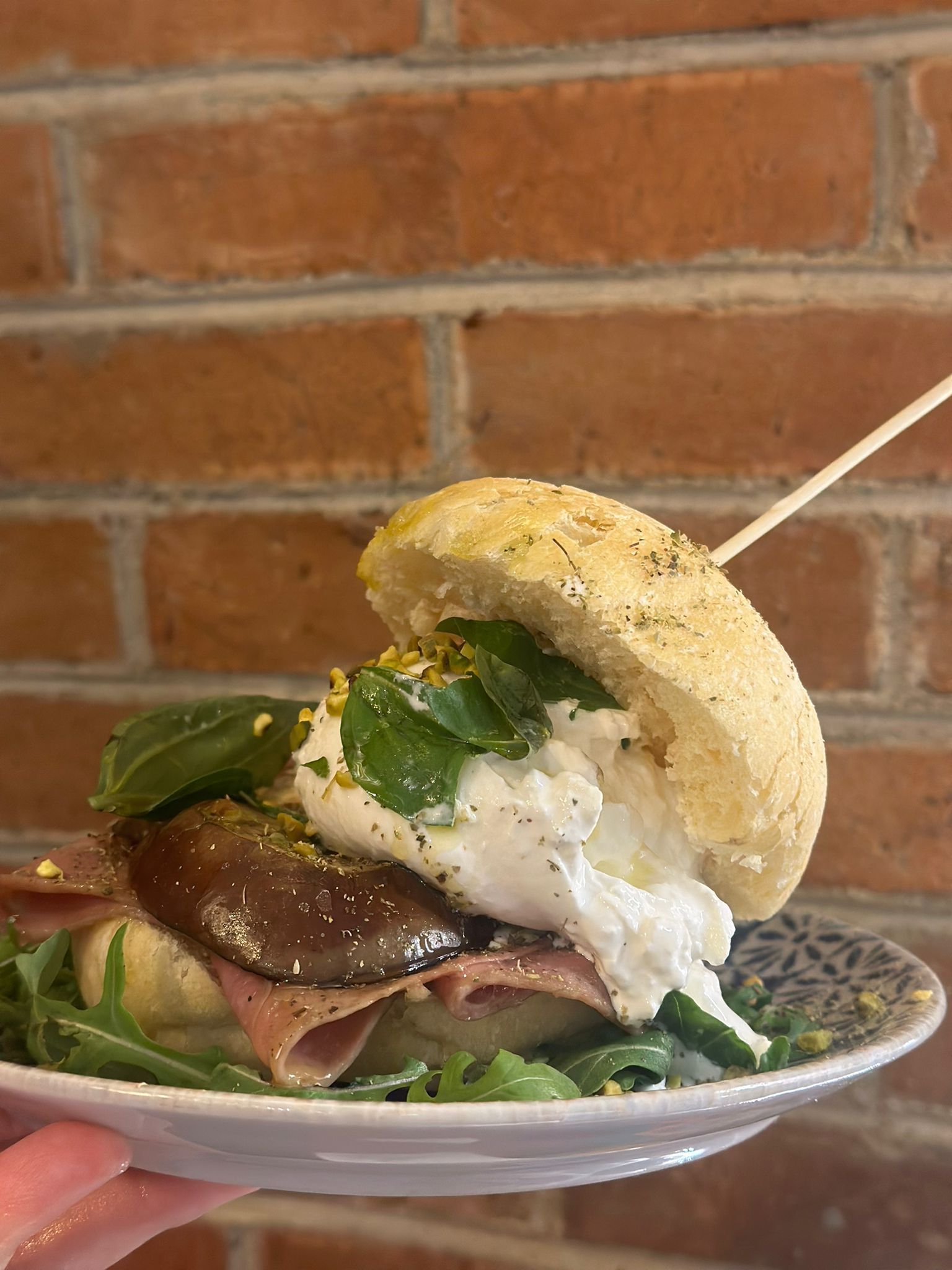 Una persona tiene in mano un piatto di cibo con un panino sopra.