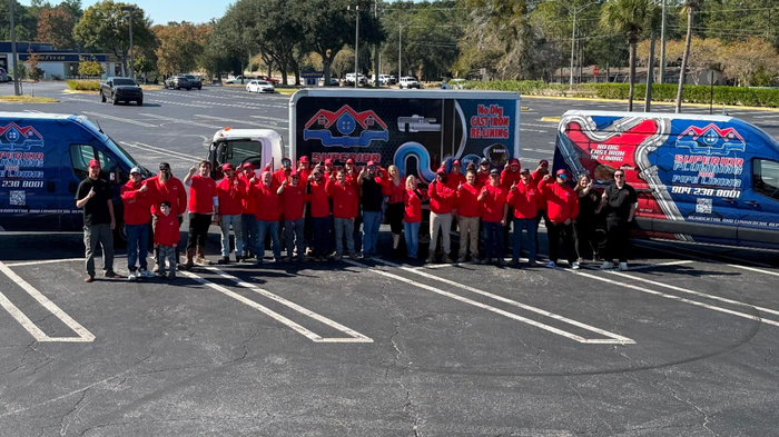 Large group of people in red shirts pose with moving trucks in a parking lot.