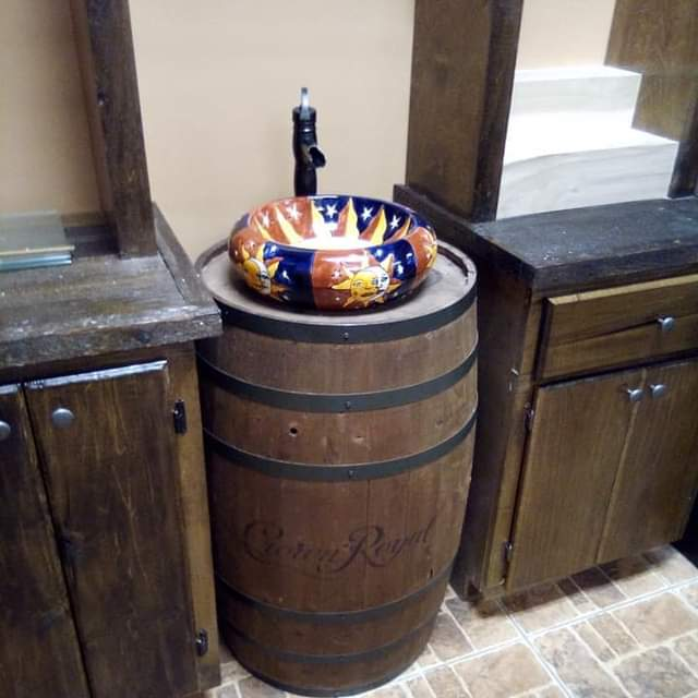 A Crown Royal whiskey barrel used as a bathroom vanity with a colorful sun-patterned ceramic vessel sink and dark faucet.
