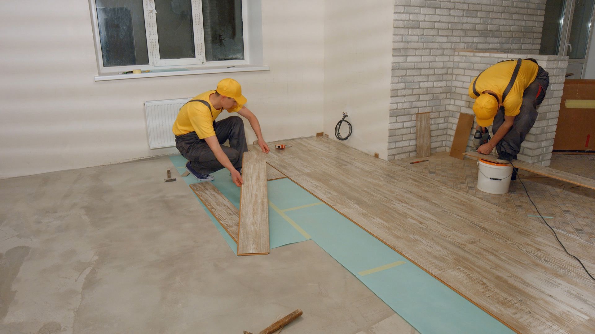 Builders laying wooden laminate boards on floor.