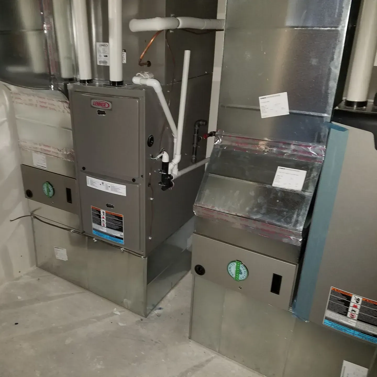 A stainless steel furnace is sitting next to another stainless steel furnace in a room.