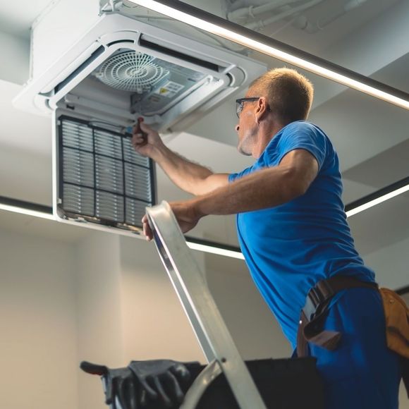 A man in a blue shirt is working on a ceiling fan.