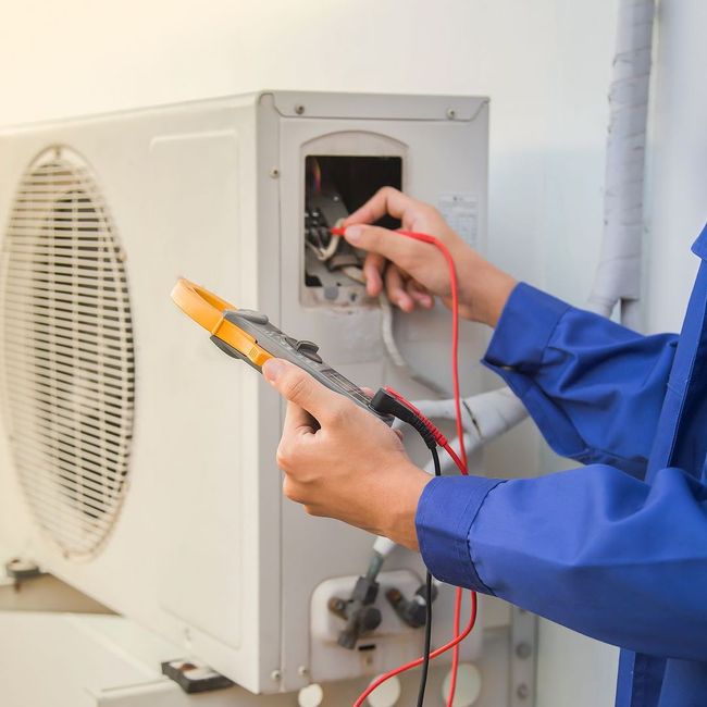 A man is working on an air conditioner with a multimeter.