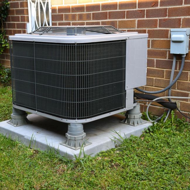 An air conditioner is sitting on a concrete base in front of a brick wall