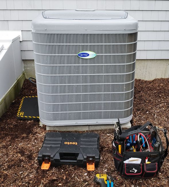A large air conditioner is sitting on top of a pile of mulch next to a tool bag.