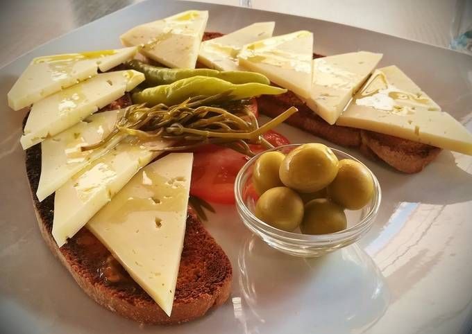 Un plato blanco cubierto con rodajas de queso, tomates y aceitunas.