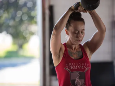 A woman is lifting a kettlebell over her head in a gym.