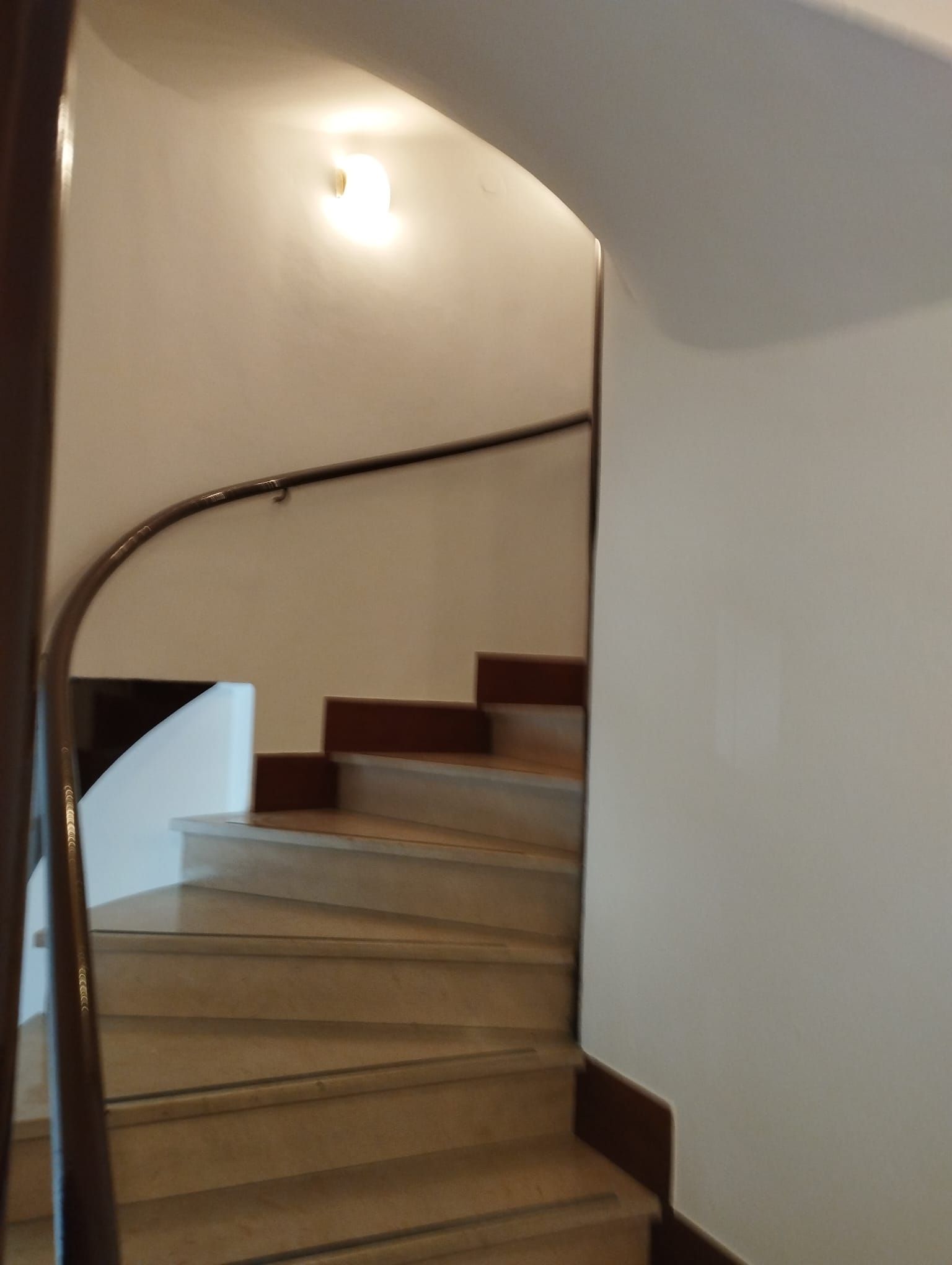 Una scala a chiocciola con ringhiera in legno e parete bianca