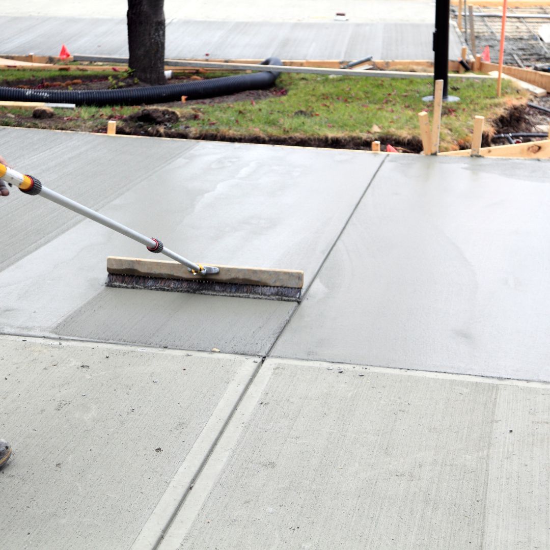 Person brushing freshly poured concrete sidewalk.