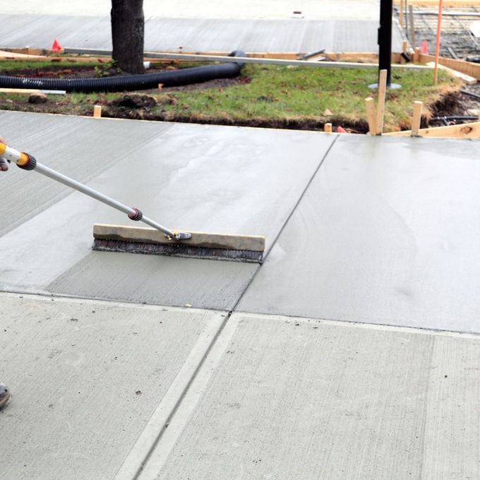Freshly poured concrete sidewalk being finished with a broom.