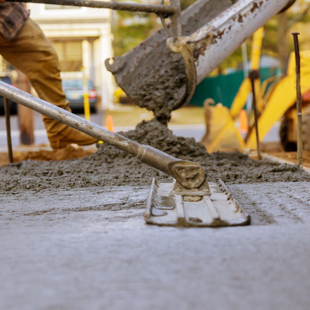 Concrete being poured onto a street, with a worker using a screed tool.